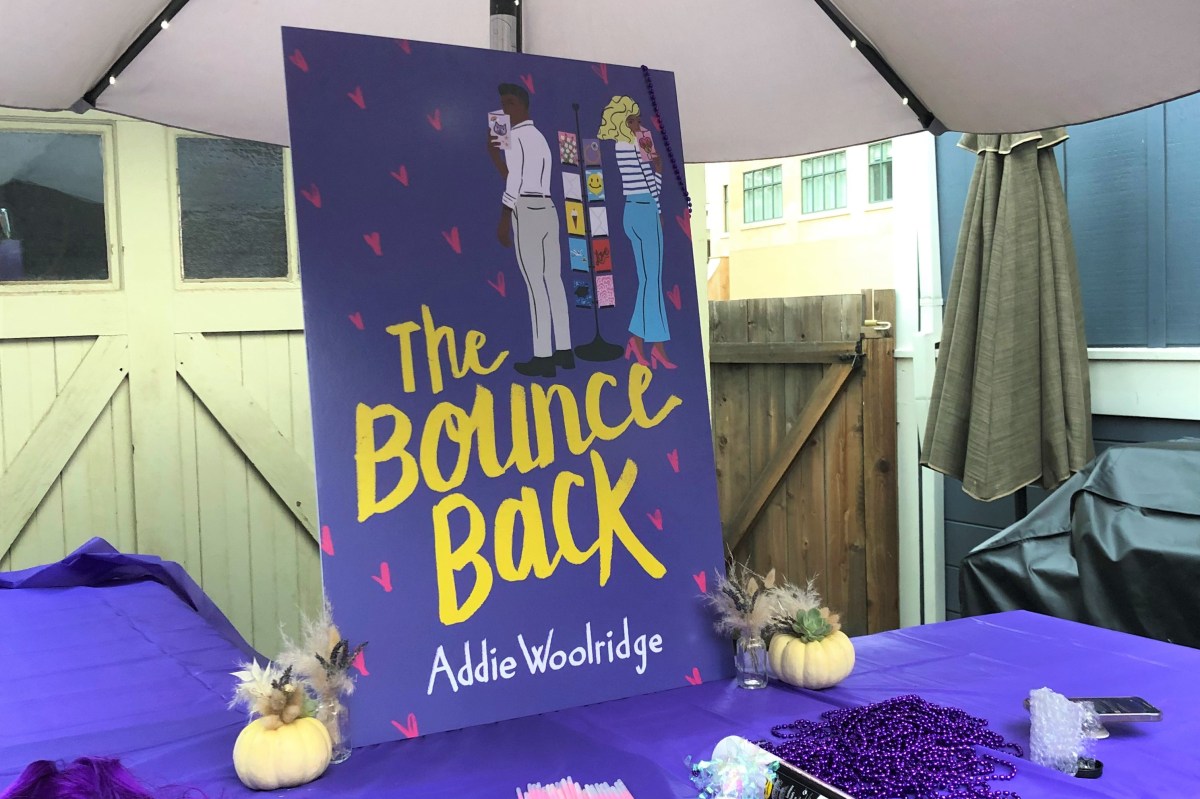 The cover of the book, The Bounce Back is blown up on a poster board that is displayed on a table under a while umbrella